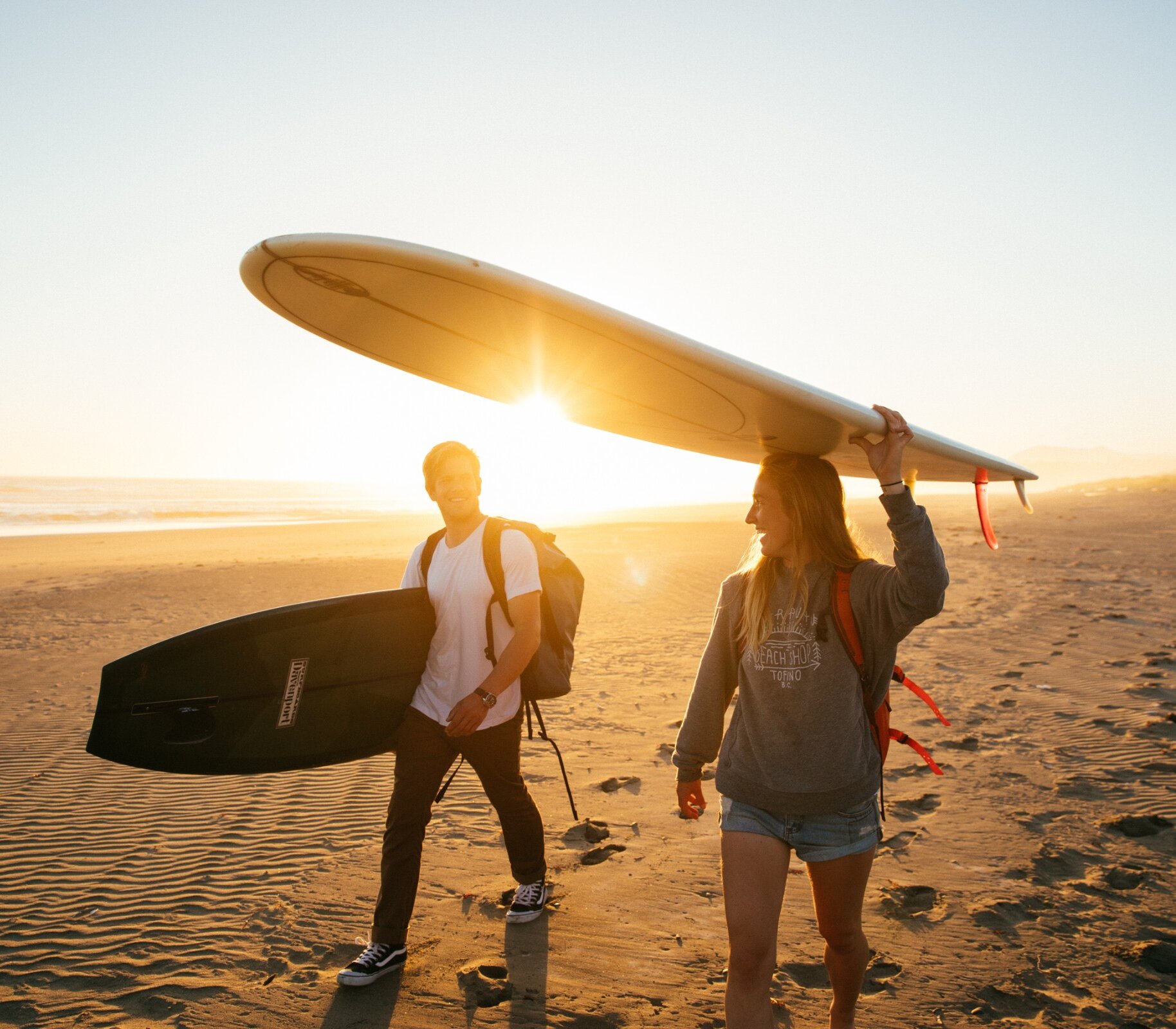 People walking with their boards on the beach with the sunset in the background