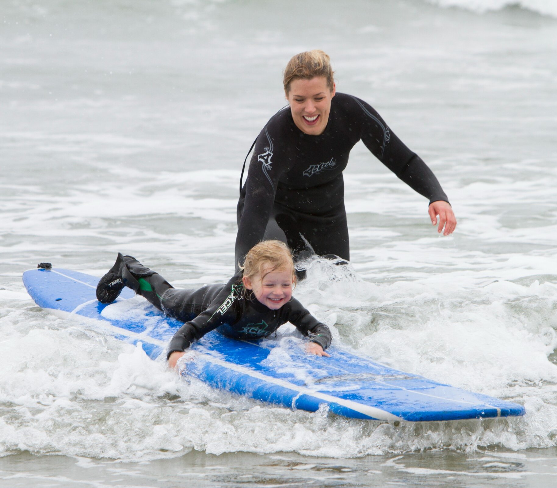 Small child laying down on a board riding a small wave with their parent holding onto the board