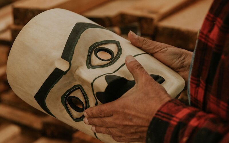 Holding a wooden carving of a mask in a workshop