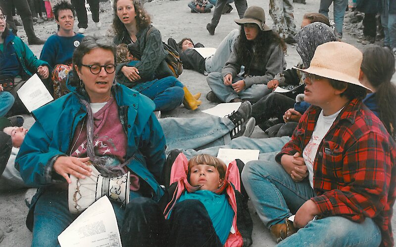 Protesters peacefully sitting in protest with a Protectors of Mother Earth sign in the background
