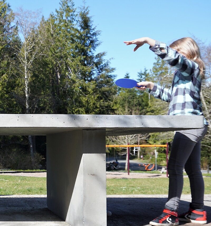 Child playing ping pong at an outdoor ping pong table.