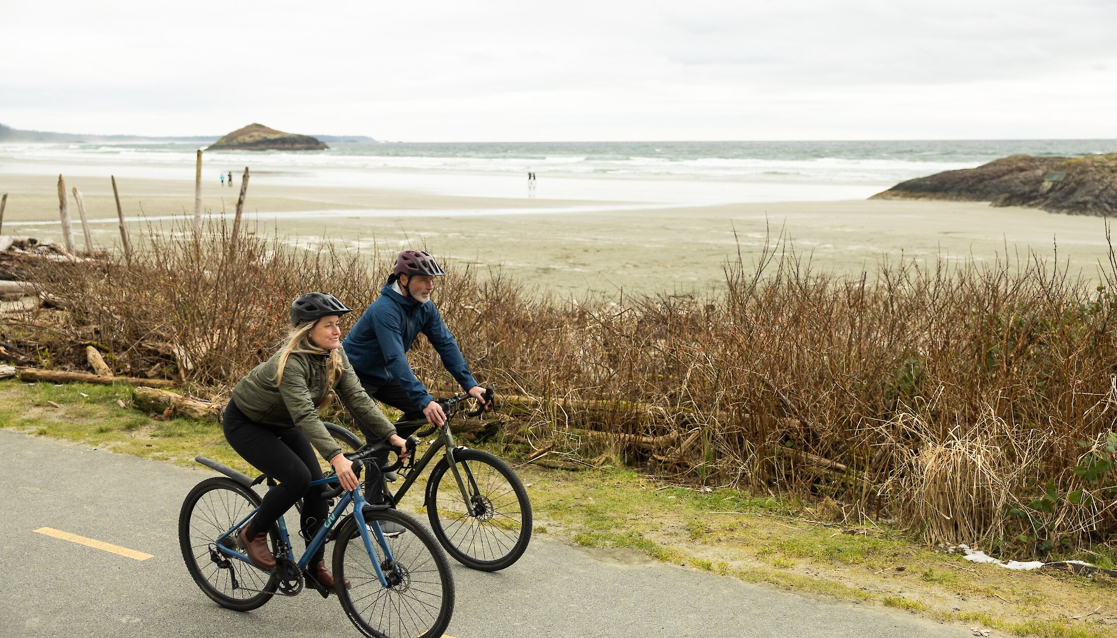 Man and woman cycling on a paved path next to Long Beach in Pacific Rim National Park Reserve