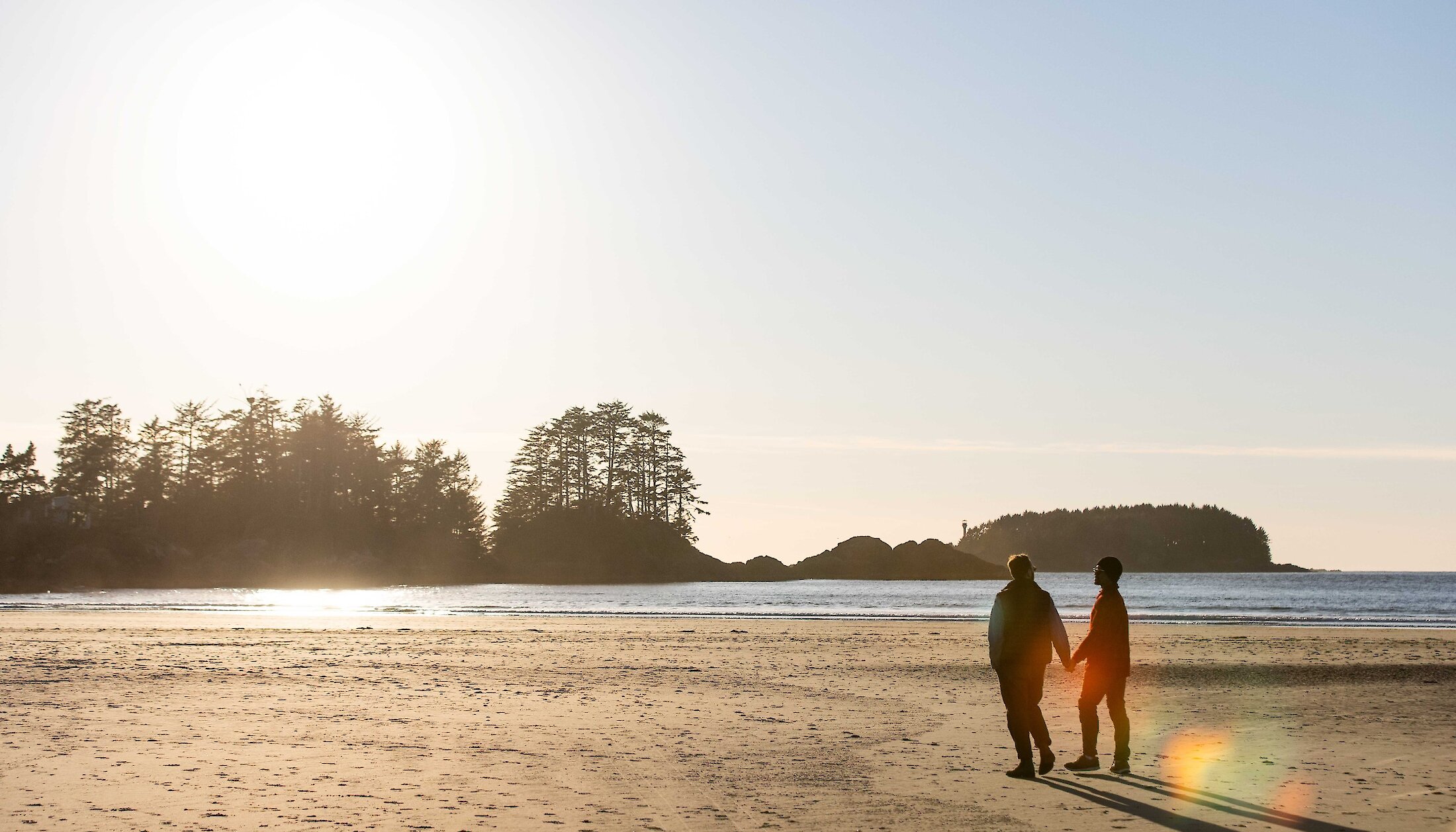 Same sex male couple walking on sandy beach in afternoon sun