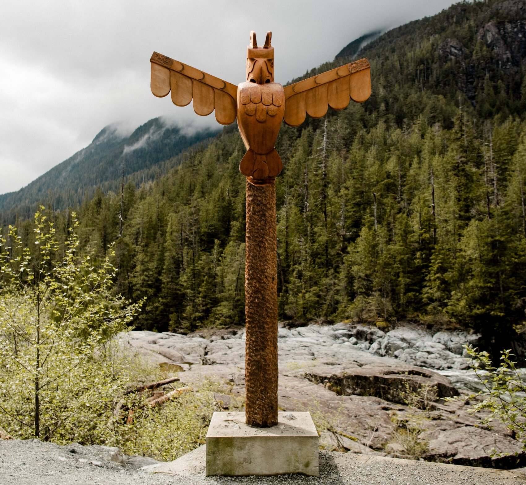 Totem pole set amongst the background of a river and a forested mountainside