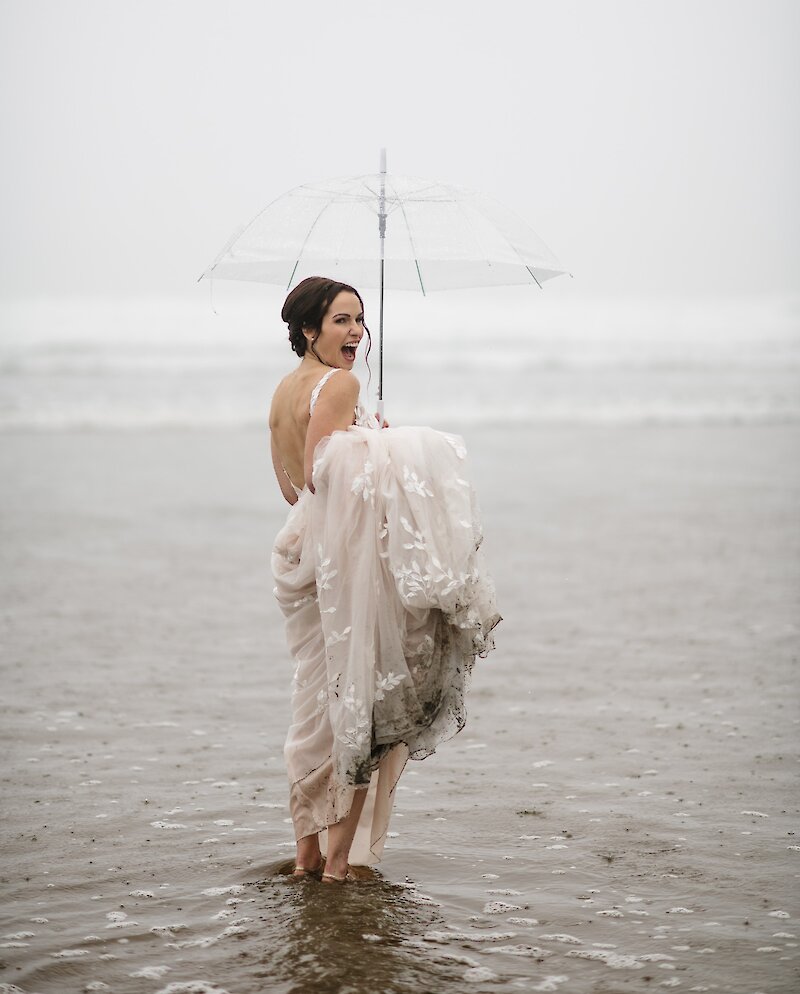 Smiling bride holding umbrella and standing in ocean