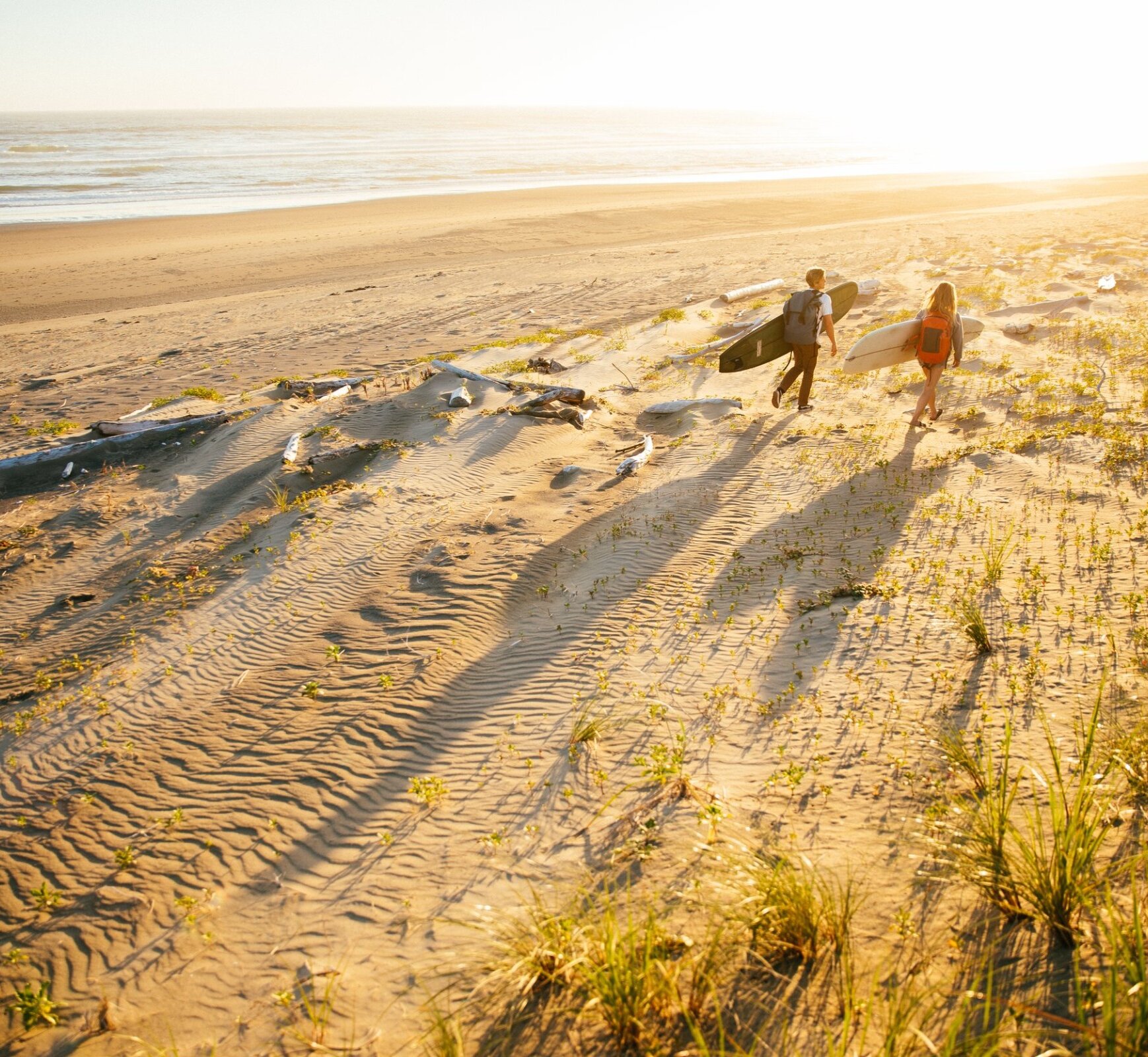 People walking along the beach with surfboards and backpacks