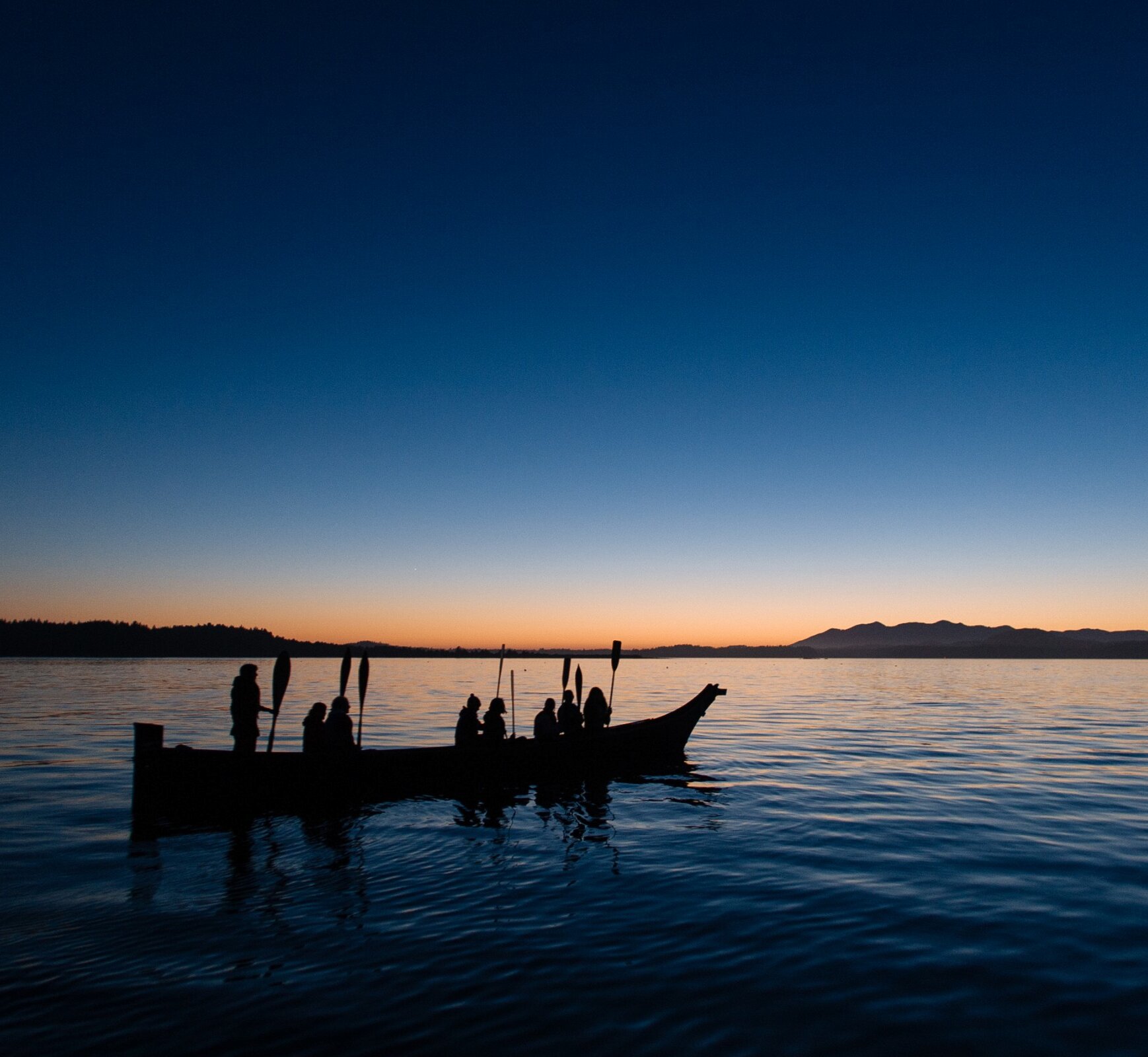 First Nations paddlers in a dug out canoe at sunset