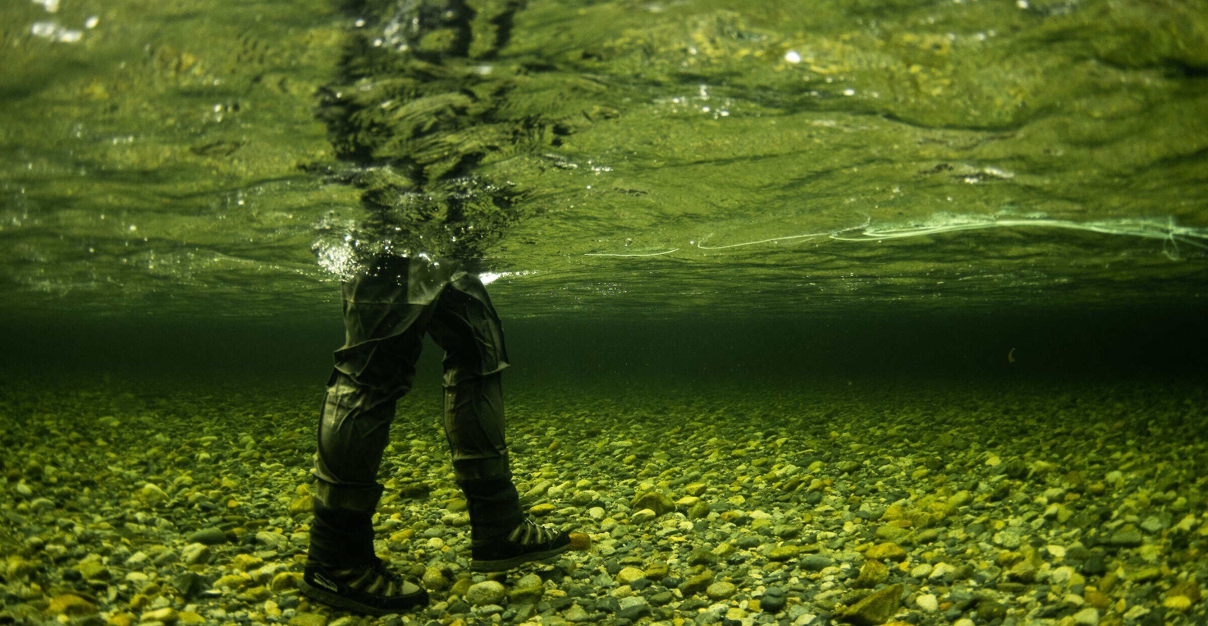 Underwater image of a person with hip waders on fly fishing in the river