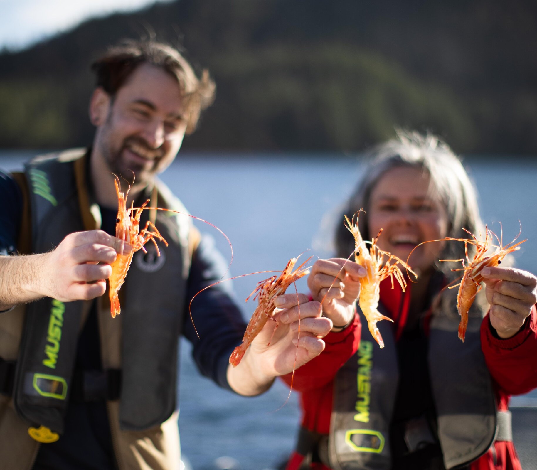 Two people on a boat holding fresh prawns in their hands