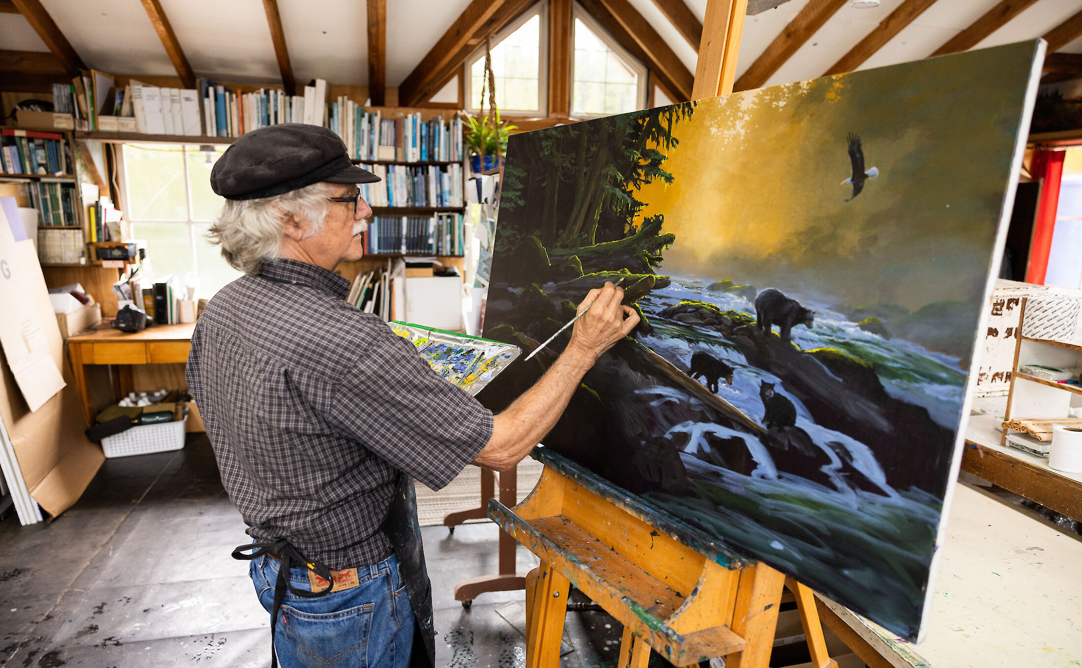 Artist Mark Hobson wearing a hat and painting at an easel