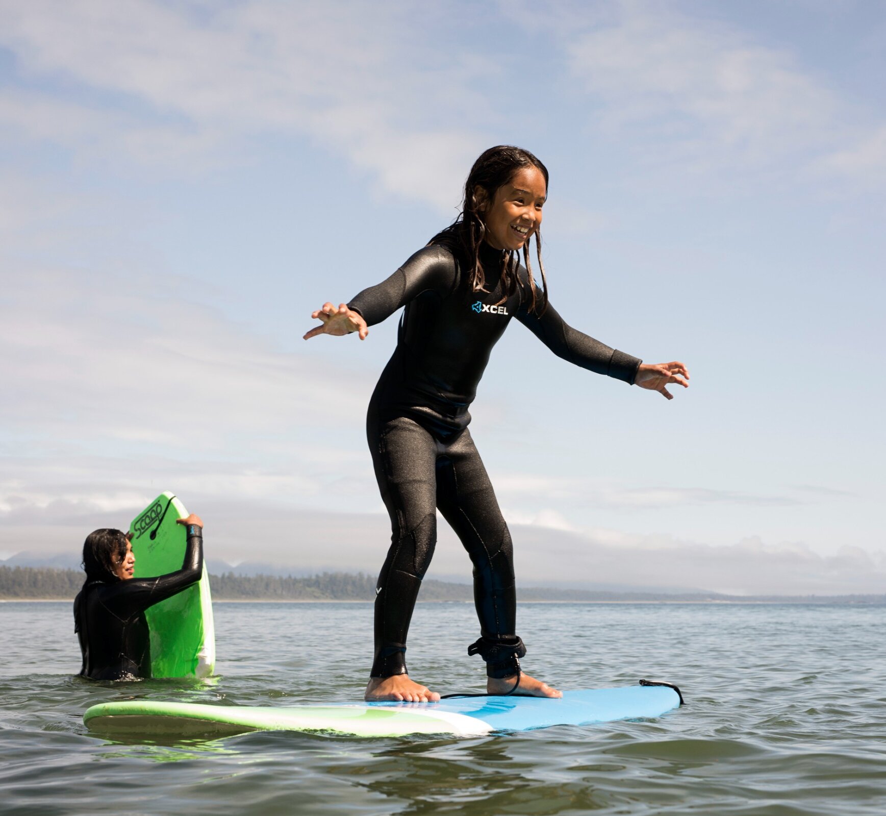 Child standing on a surfboard with their parent in the background