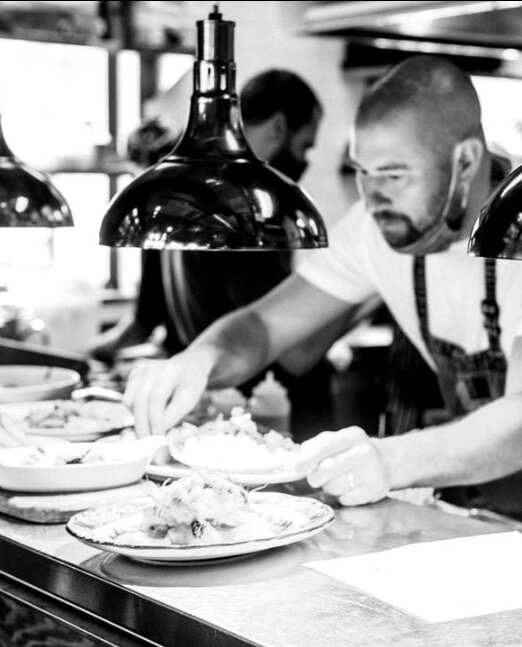 Chef Nick Nutting wearing an apron and at work plating dishes.