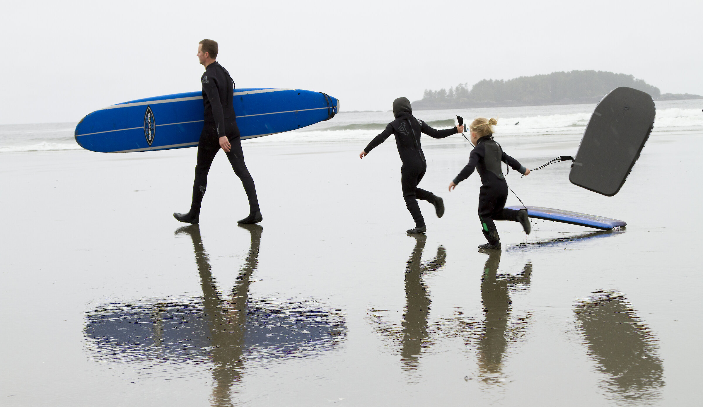 Father and children walking into ocean with surfboard and boogie boards
