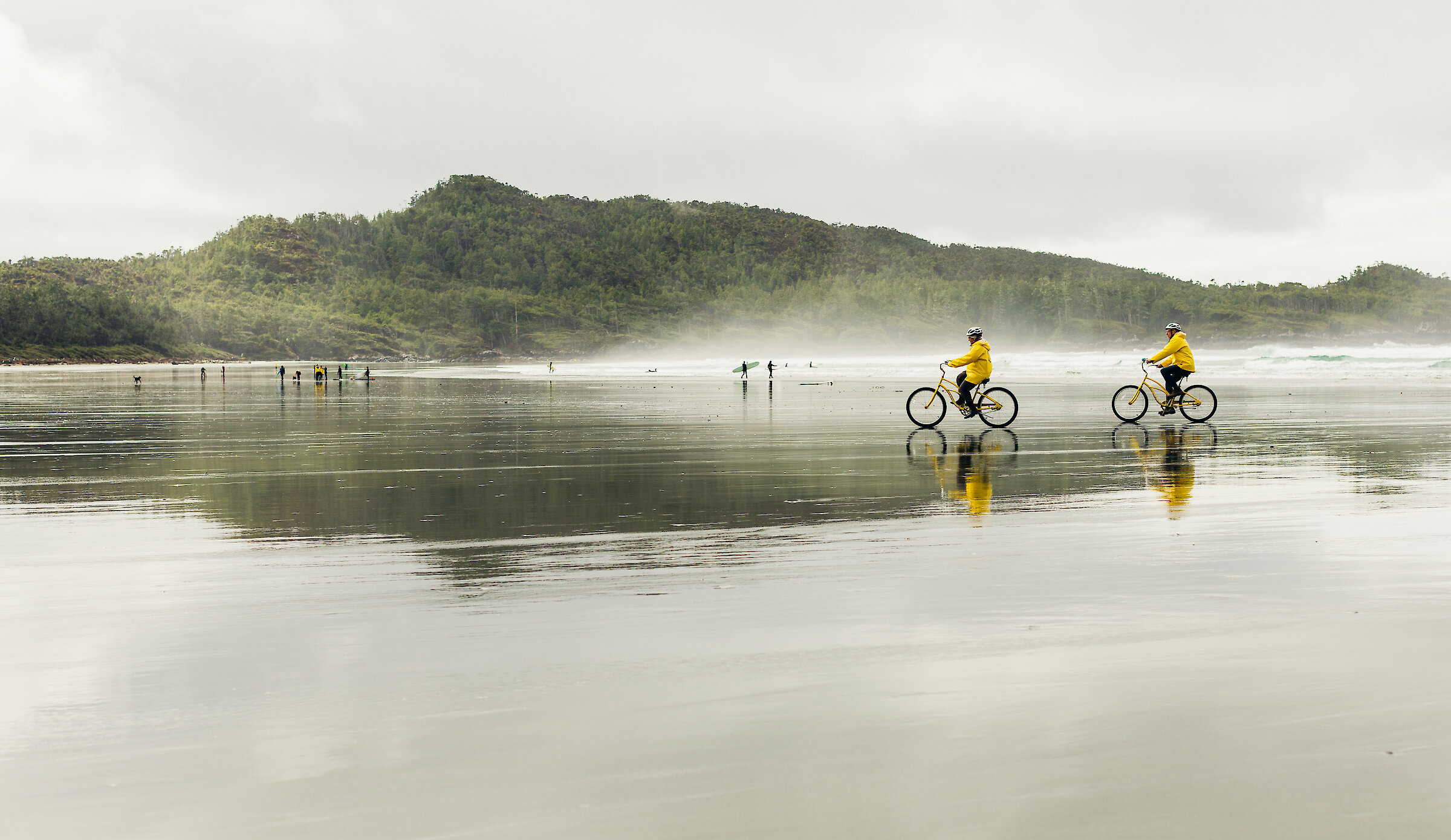 Two people wearing yellow raincoats and cycling on a rainy beach