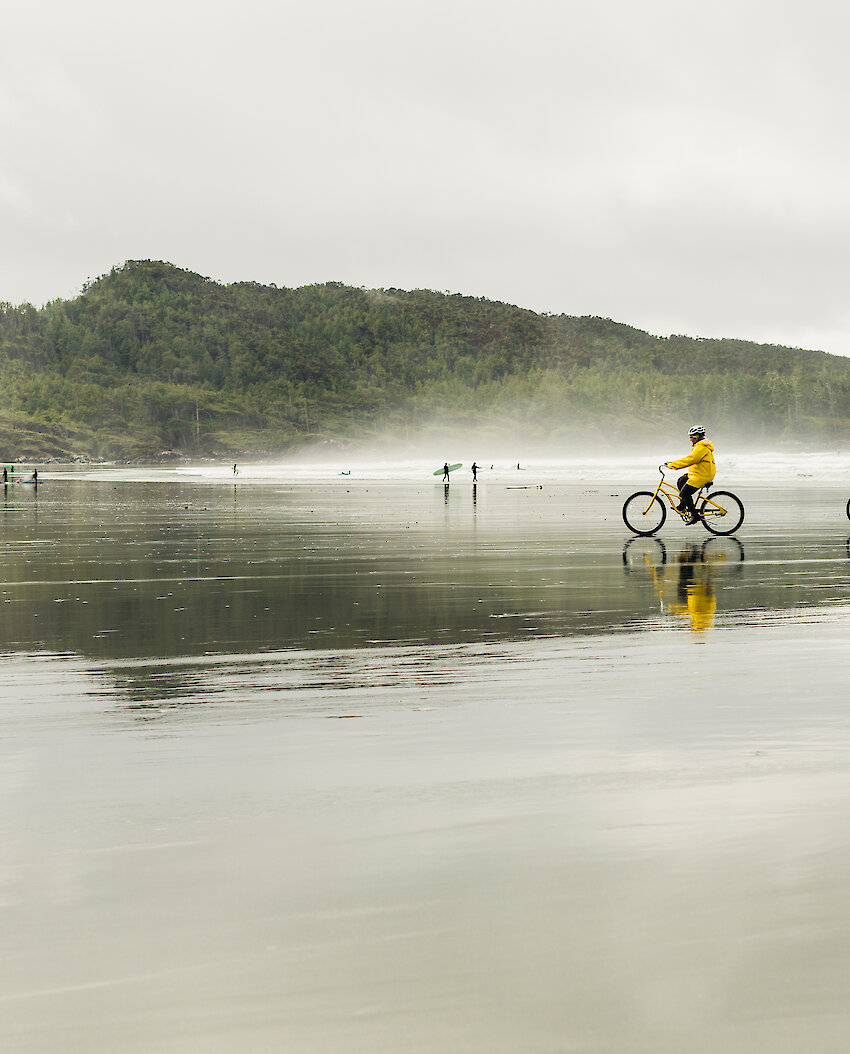 Two people wearing yellow raincoats and cycling on a rainy beach