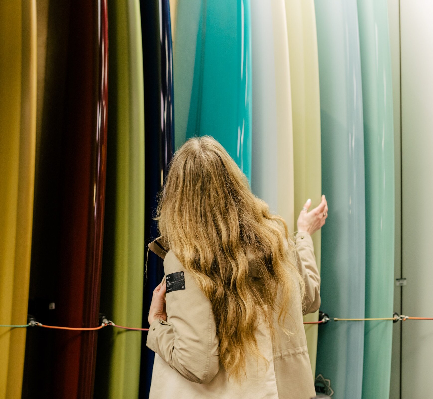 Woman with long hair looking at a display of colourful surfboards
