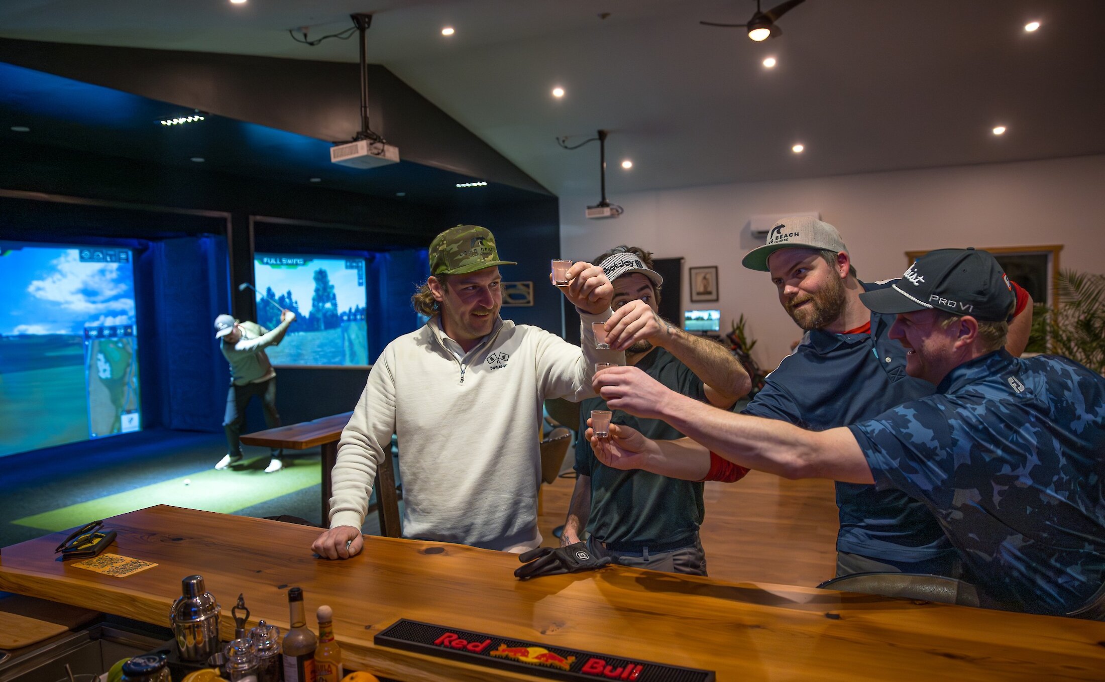 People having drinks at the bar inside the Long Beach Golf Course Pro Shop, by the golf simulators.