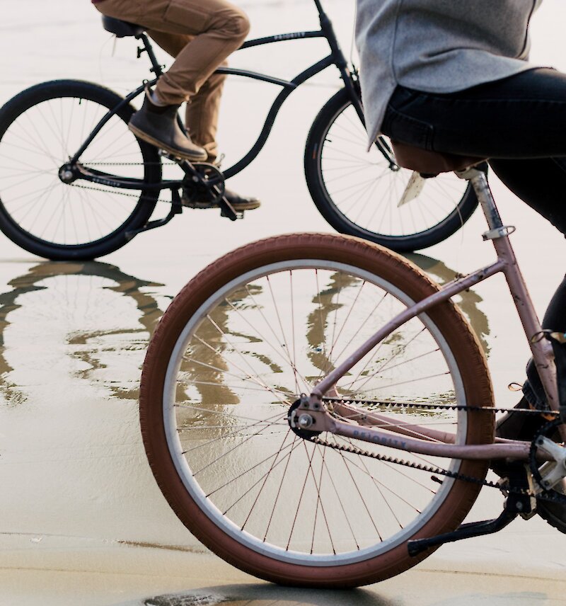 Close up of peoples' legs biking on the wet beach sand