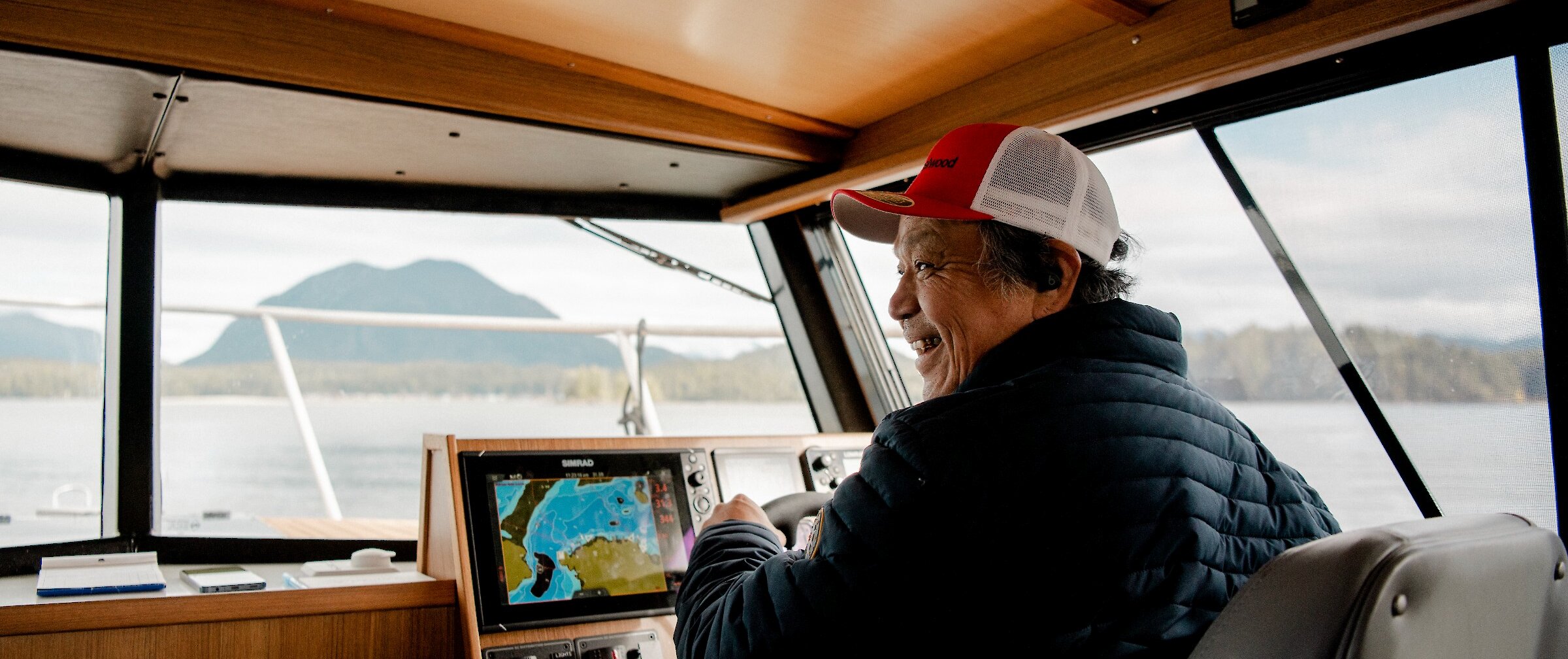 Man driving boat, smiling, with Meares Island visible in the distance.