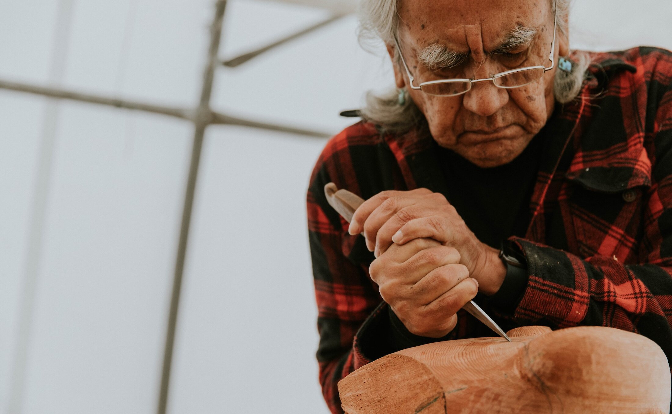 First Nations person carving a piece of cedar into a mask.