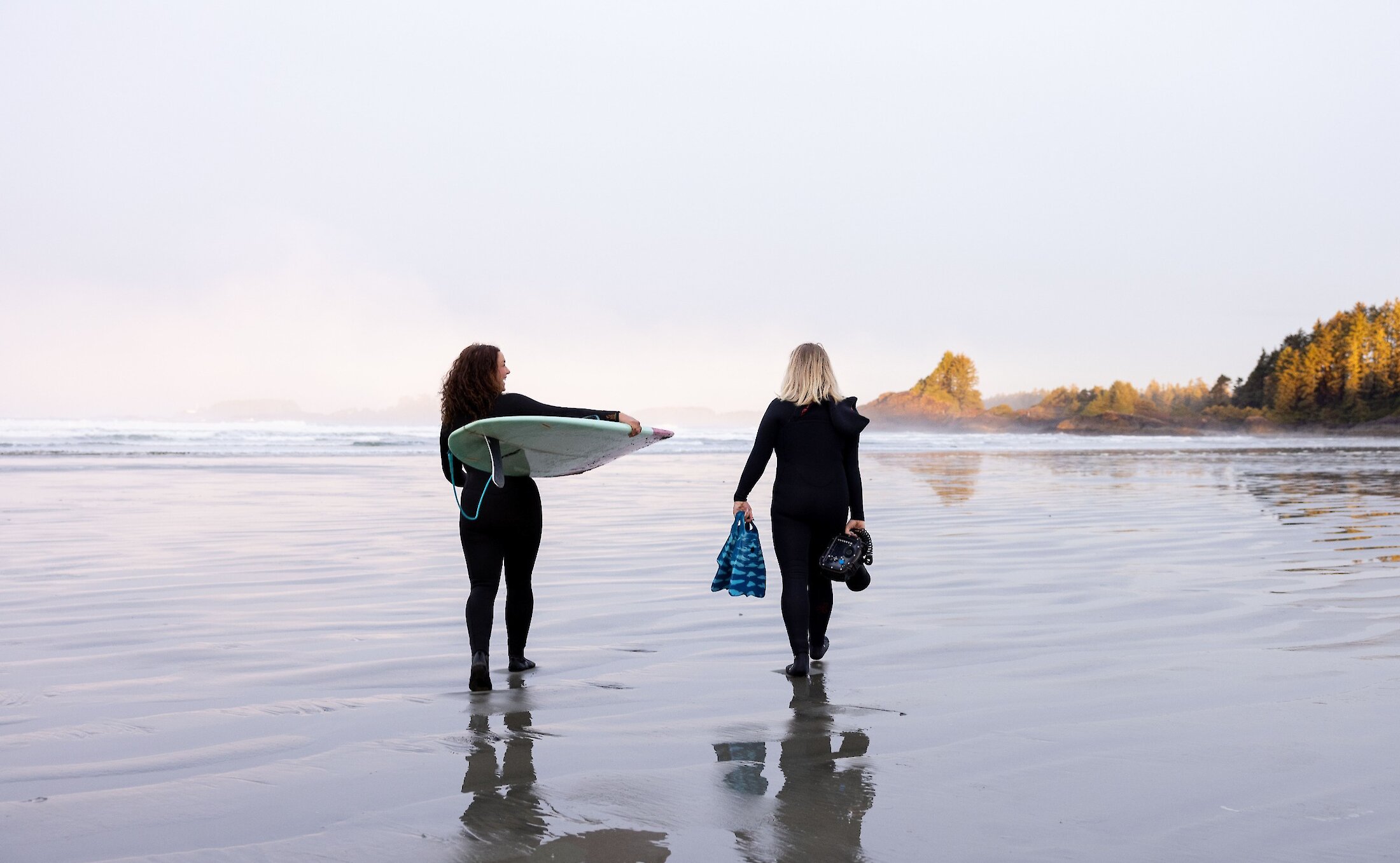 Two friends walking in wetsuits on the beach