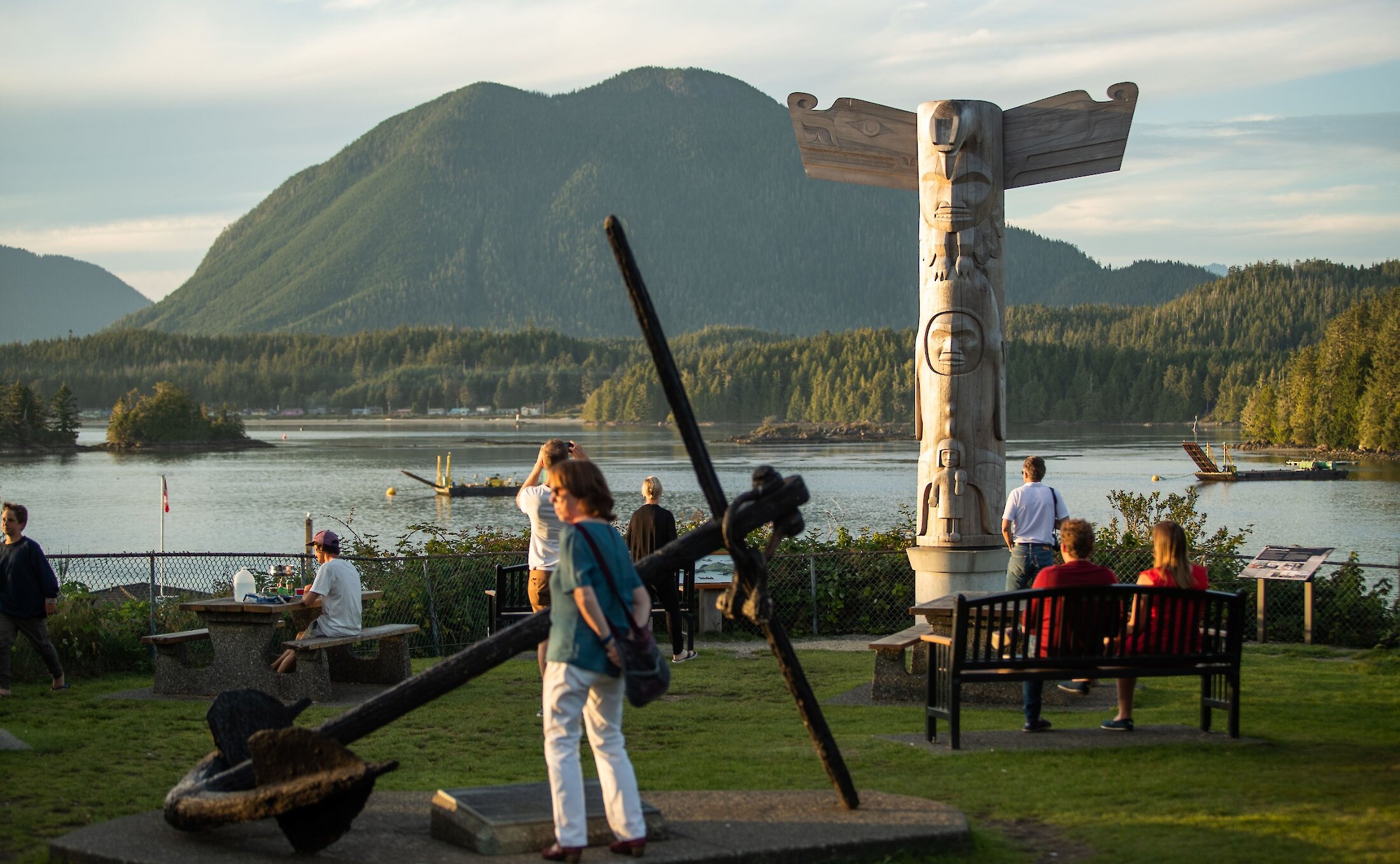 Person looking at the massive anchor on the lawn of a community park with a totem in the background