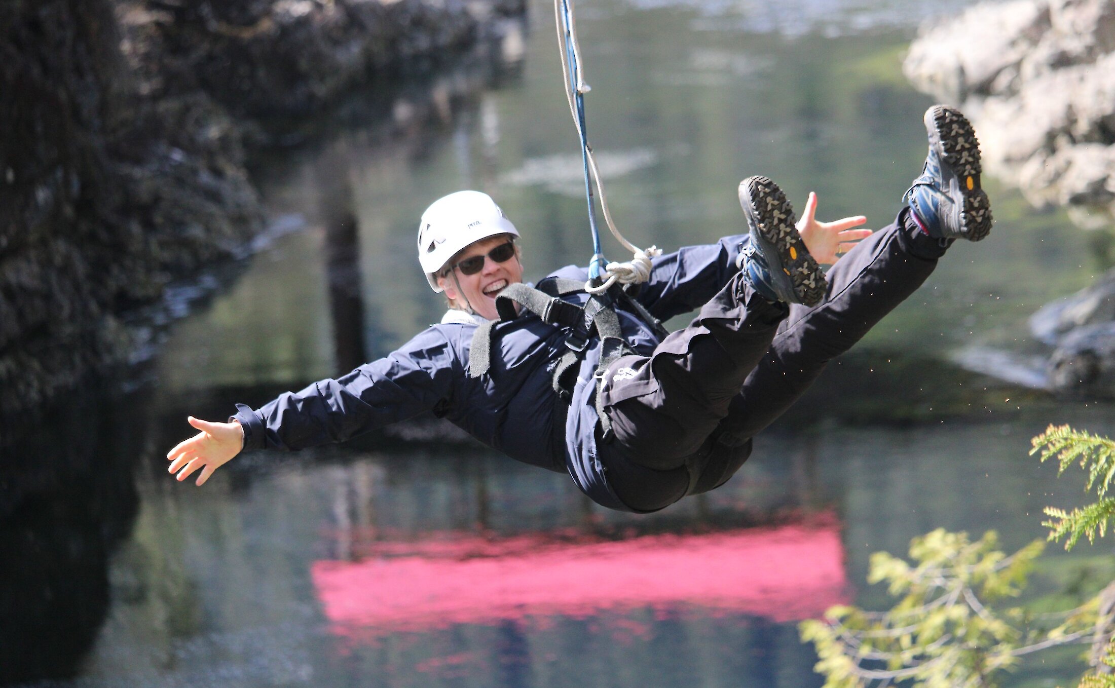 A smiling zipliner with arms held out zips over a river.