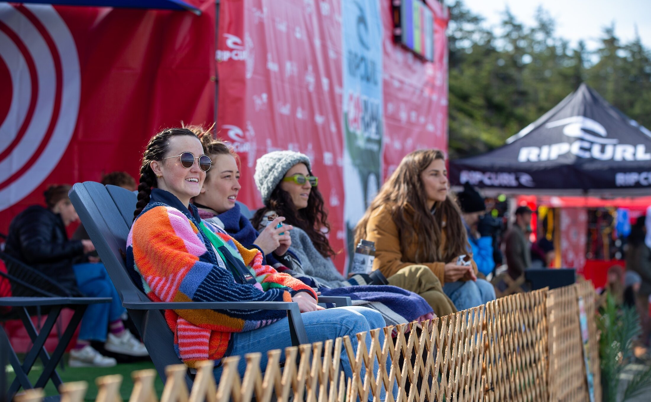 A group of women seated below the judging tower on the beach watching the Rip Curl Pro surf competition at Cox Bay.