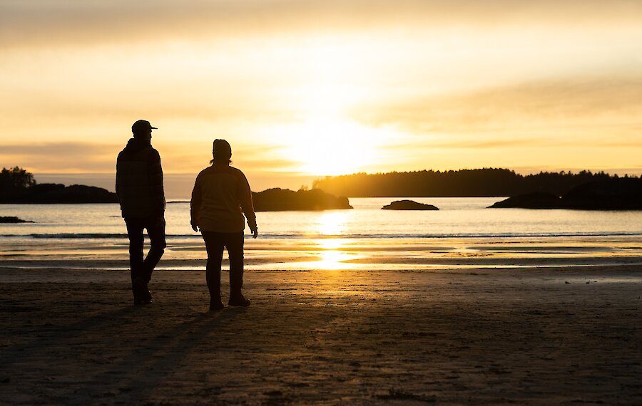 Shadows of people walking along the beach with the sunrise in the background