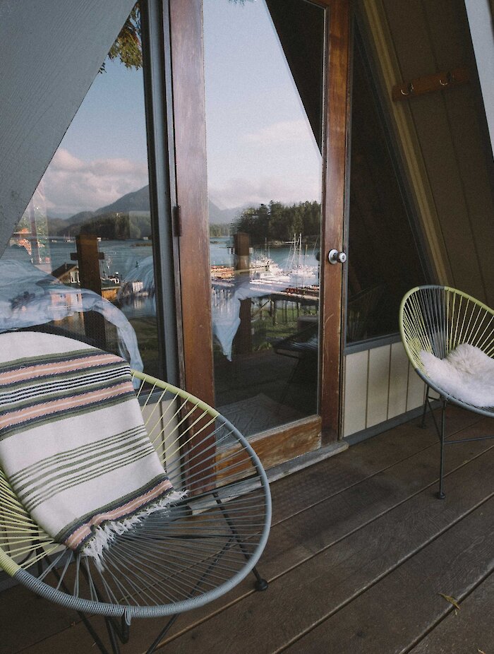 The Shoreline Tofino A-frame cabin deck with two chairs and the reflection of the Sound in the patio door window.