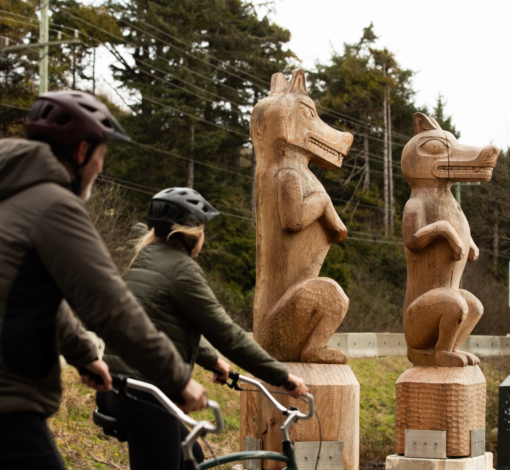 Two people biking by two wolf carvings at Incinerator Rock in the Pacific Rim National Park Reserve