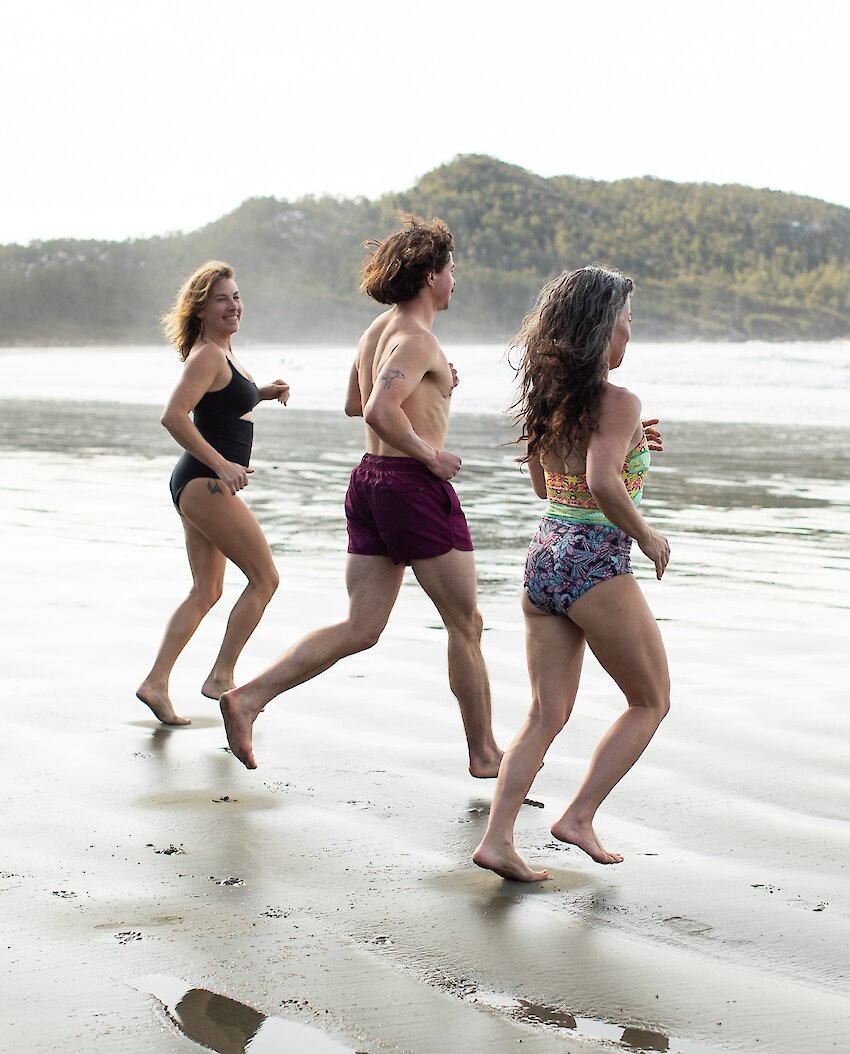 Three friends in swimsuits running into the ocean