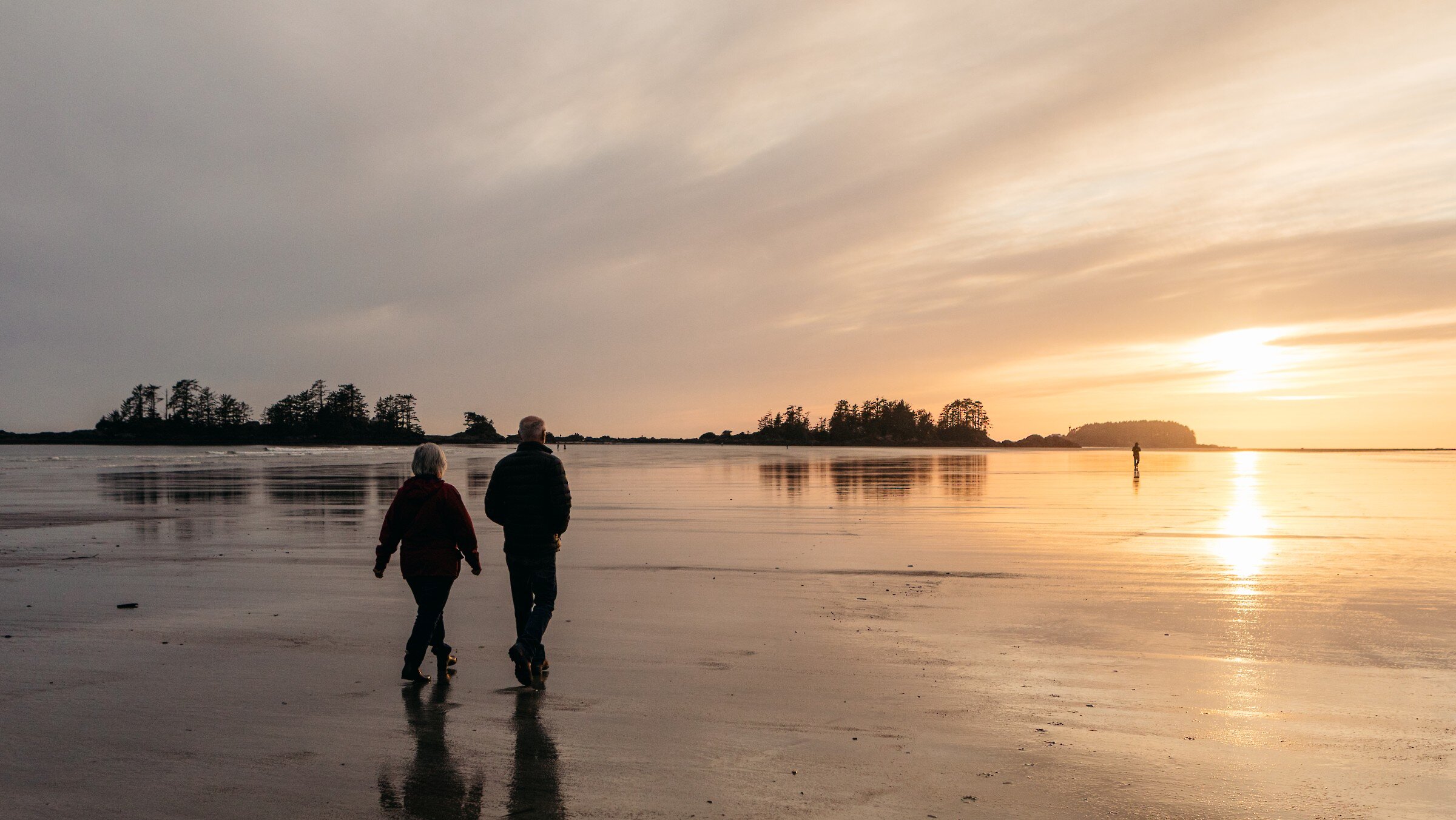 Silhouettes of two people walking at sunset toward view of Frank Island and North Chesterman Beach
