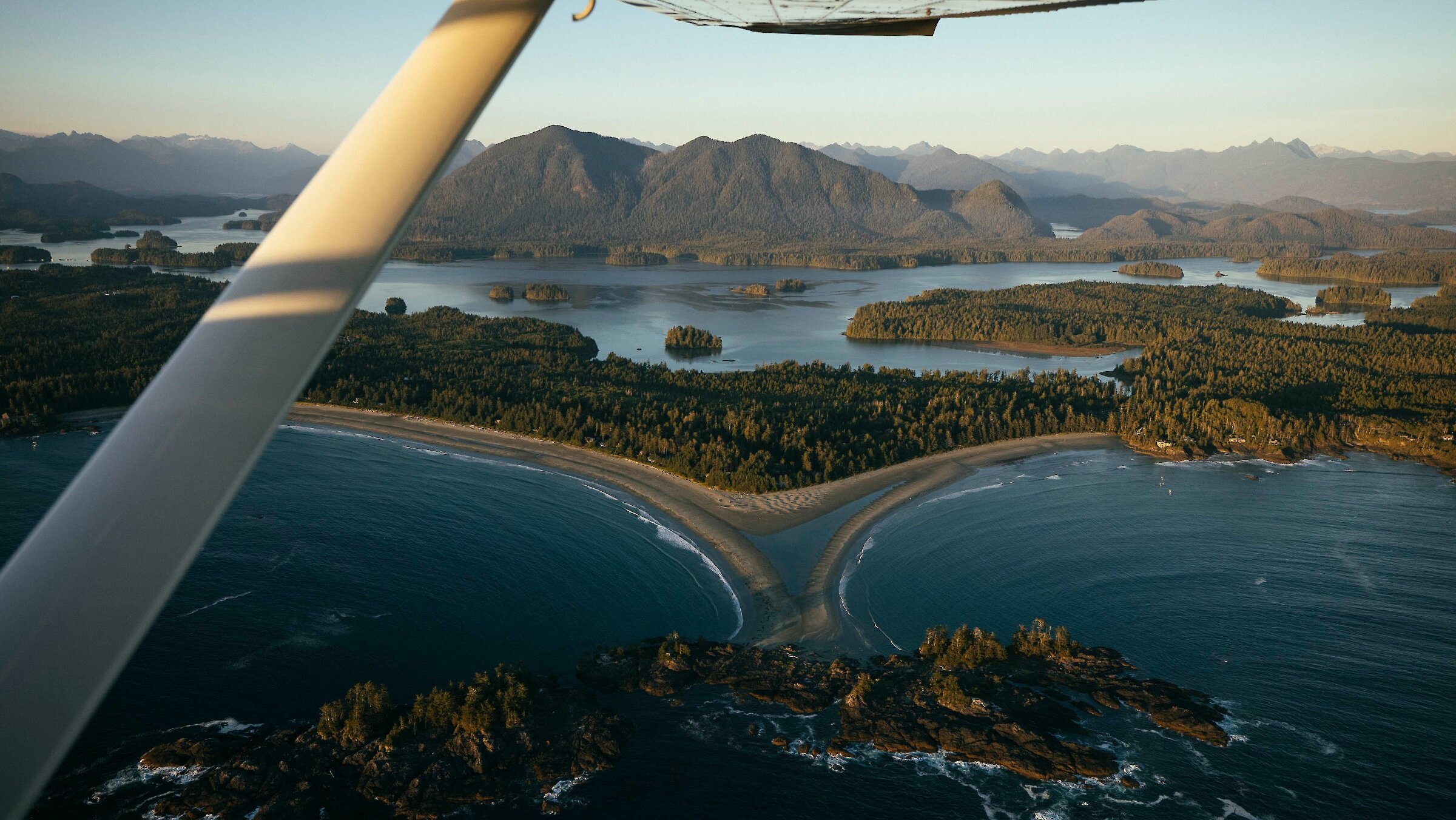 View out the window of a place of two beaches, a sand spit connected to an island, and coastal mountains in the distance.