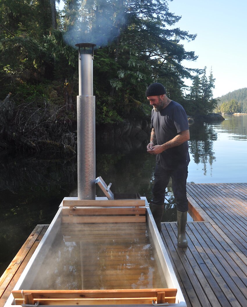 A cedar-sided wood-fired tub on a floating dock with blue skies overhead