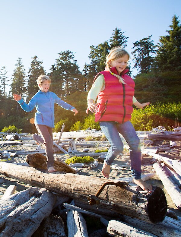 Blonde girl and boy run on a driftwood log on the beach