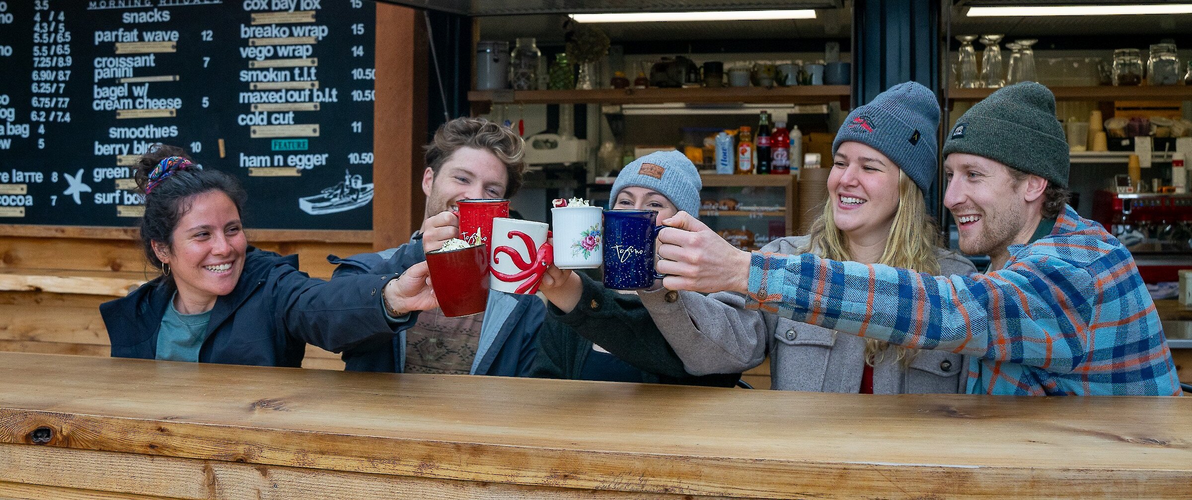 Person holding a surfboard outside of a surfshop with colourful murals on the doors