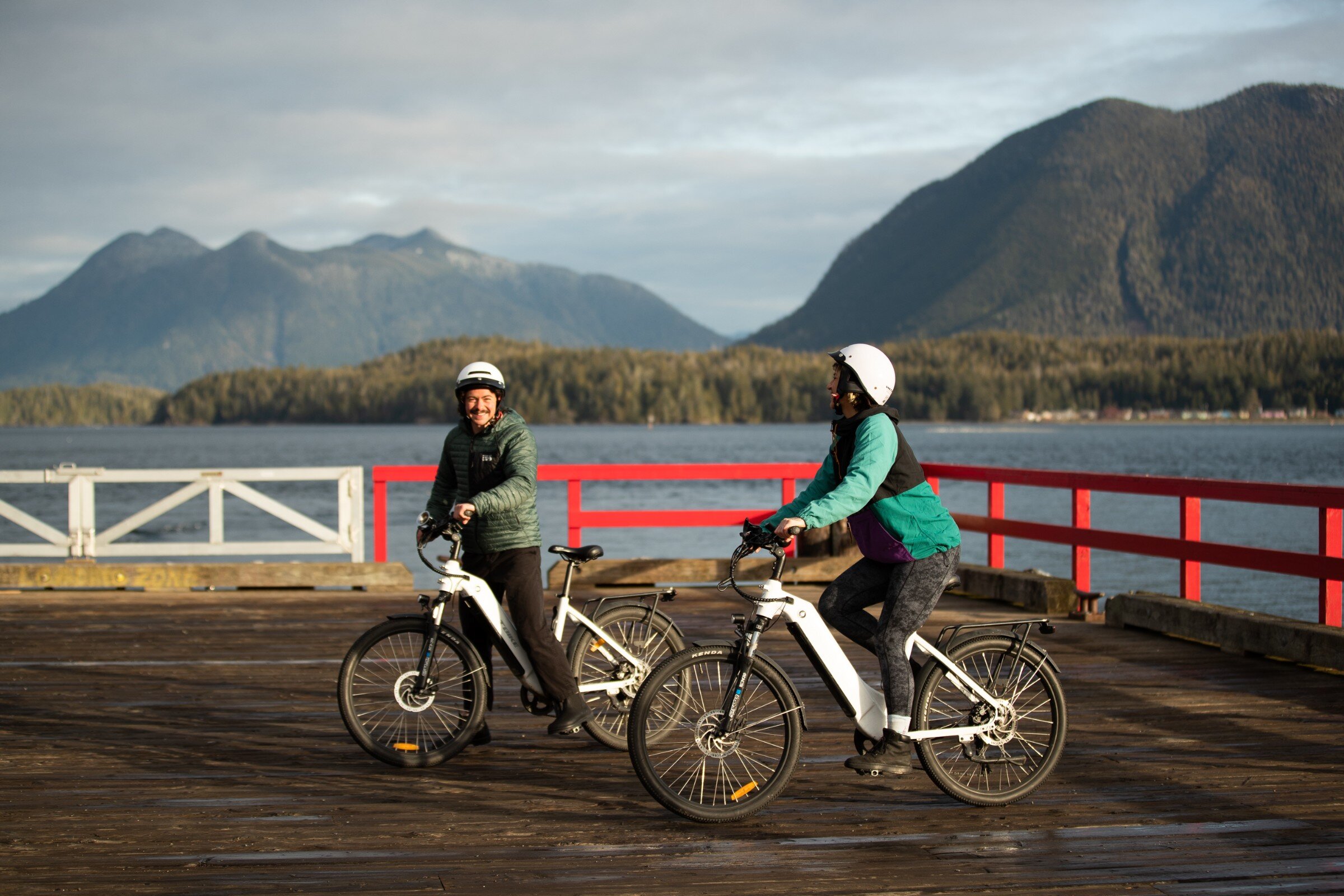 Two cyclists on First Street dock smiling with Clayoquot Sound in the background