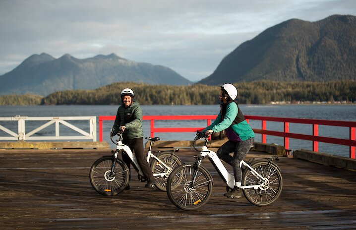 Two cyclists on First Street dock smiling with Clayoquot Sound in the background