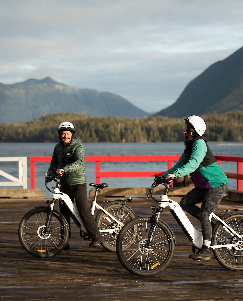 Two cyclists on First Street dock smiling with Clayoquot Sound in the background