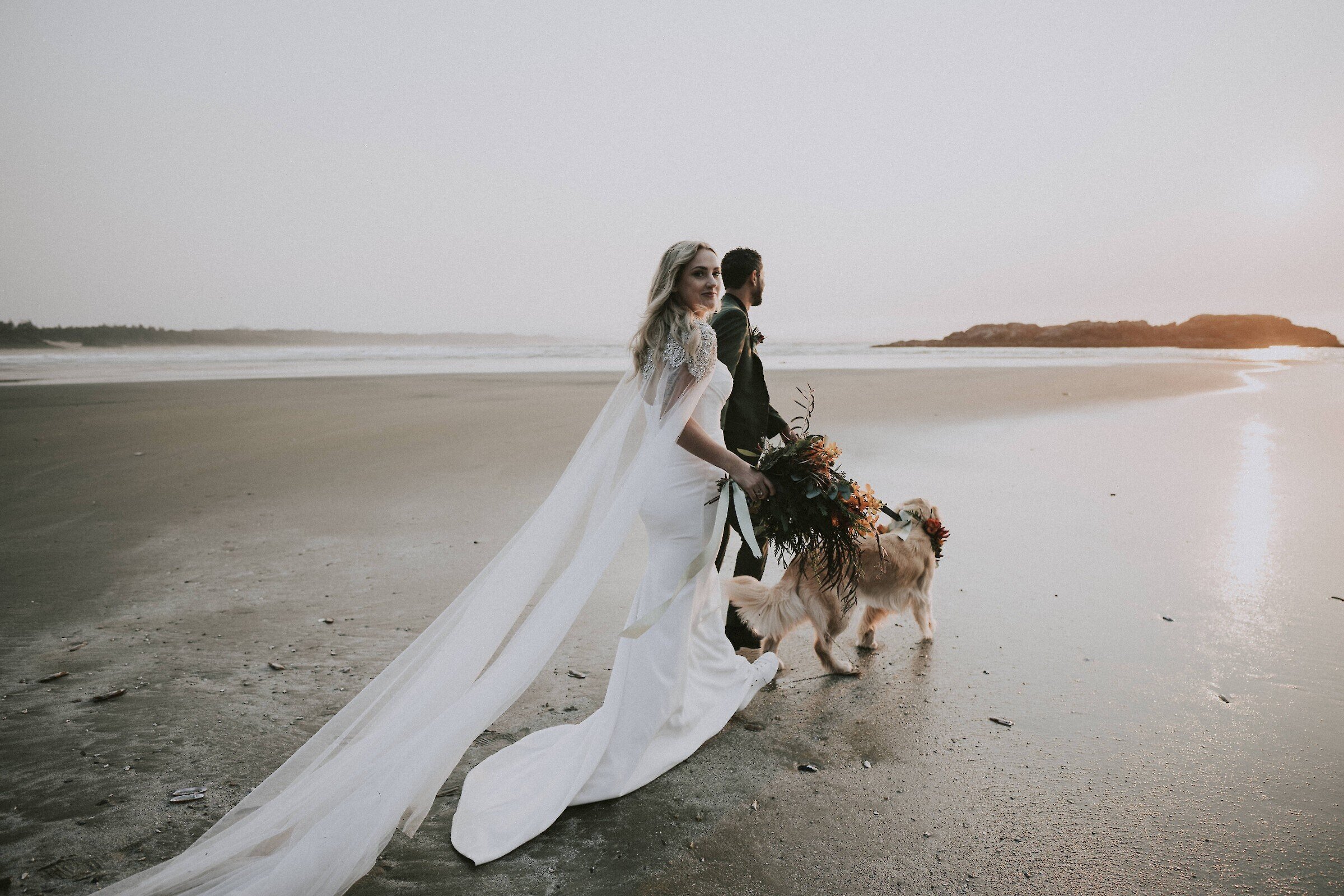 Bride, groom, and dog walking on the beach
