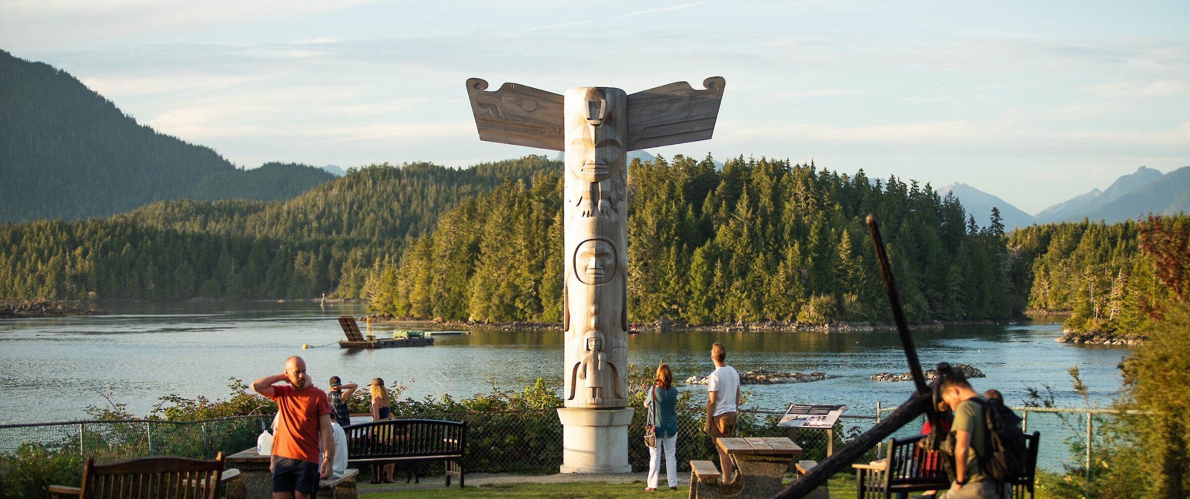 Totem pole in park with benches and picnic table, overlooking water