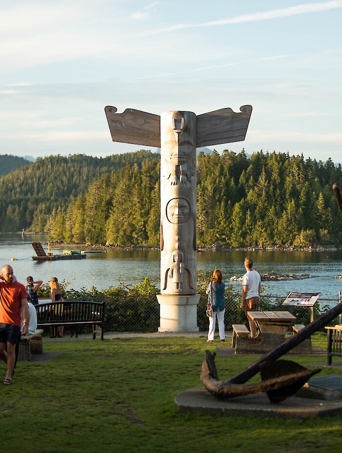 Totem pole in park with benches and picnic table, overlooking water