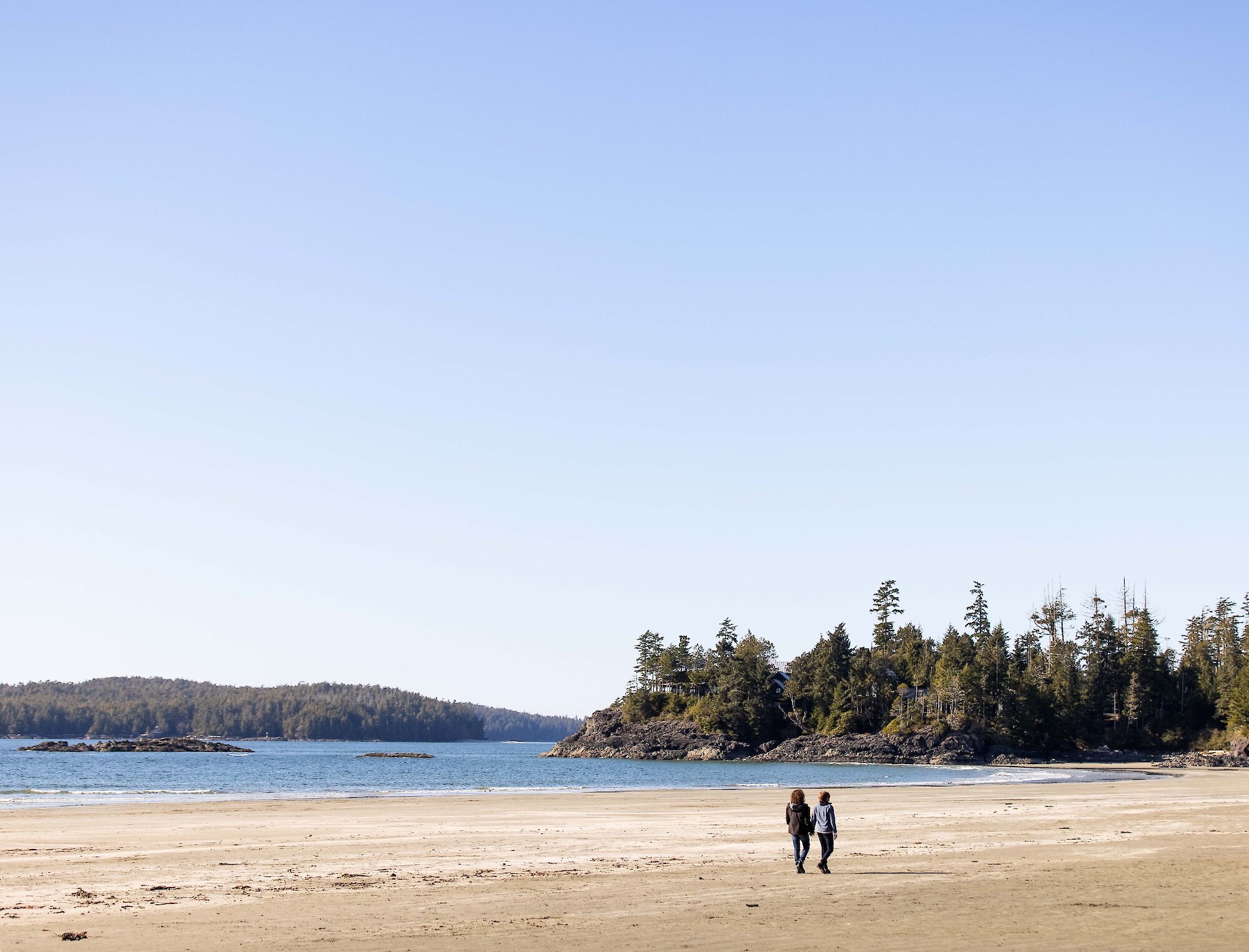 Two people walking along a sunny MacKenzie Beach