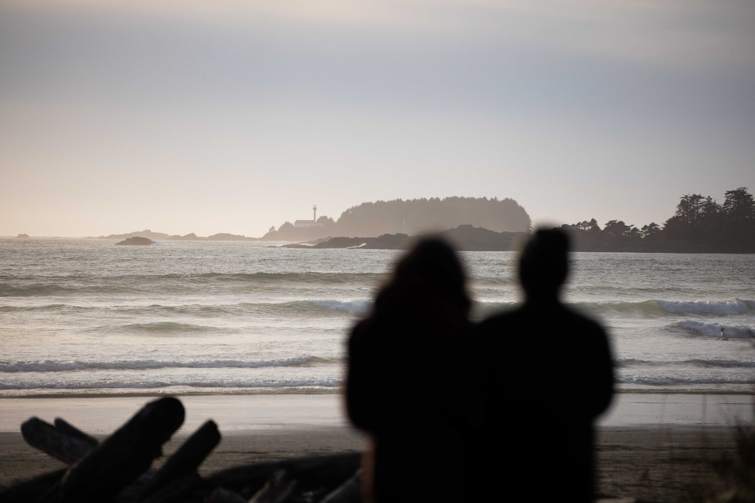 Silhouette of two people standing on Cox Bay looking out to the ocean and the distant lighthouse of Lennard Island.