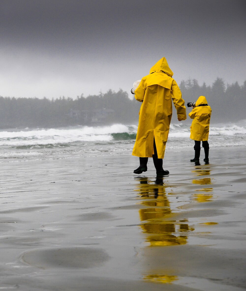 People with yellow rain slickers walking on the beach on a rainy day