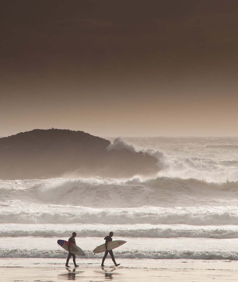 People watching on the beach with surfboards and large waves in the background