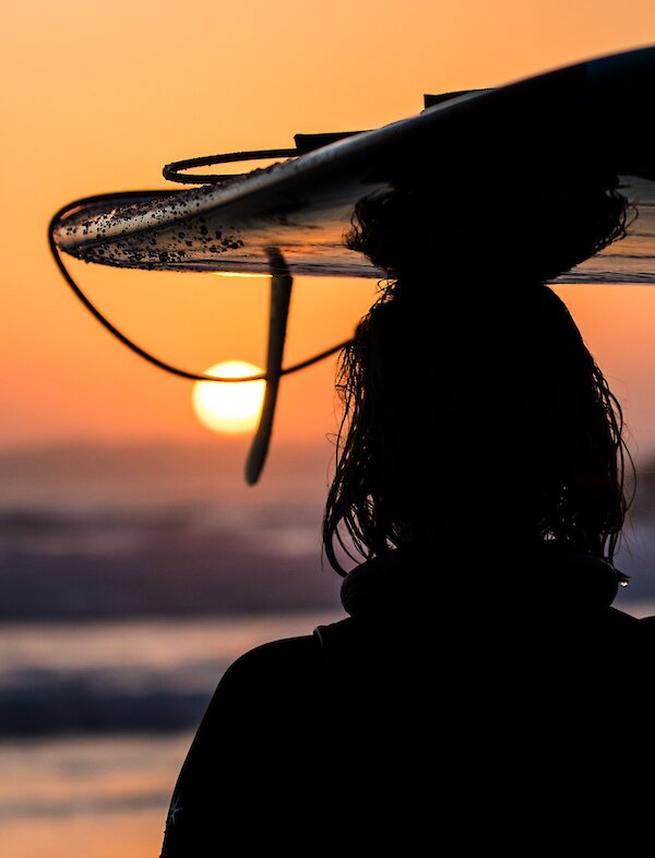 Person holding their surfboard on their head watching the sunset