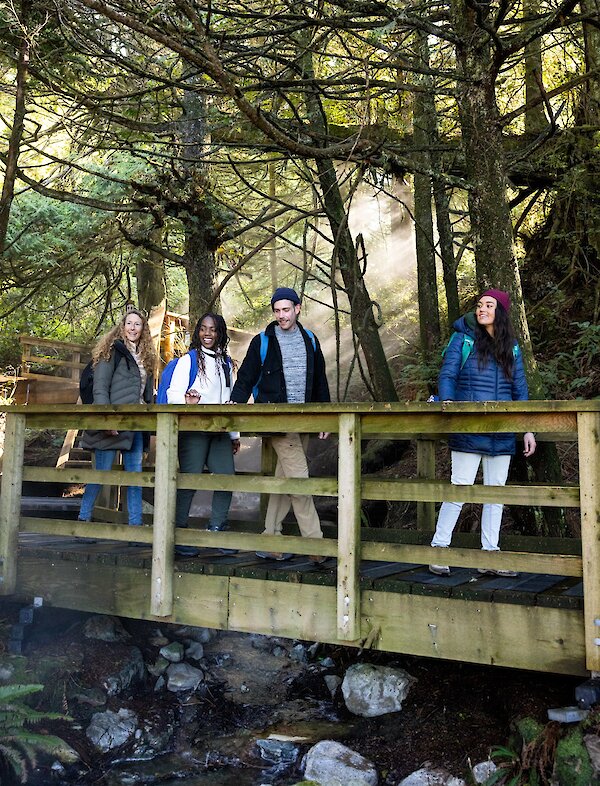 Group walking along a boardwalk over steaming water at Hot Springs Cove