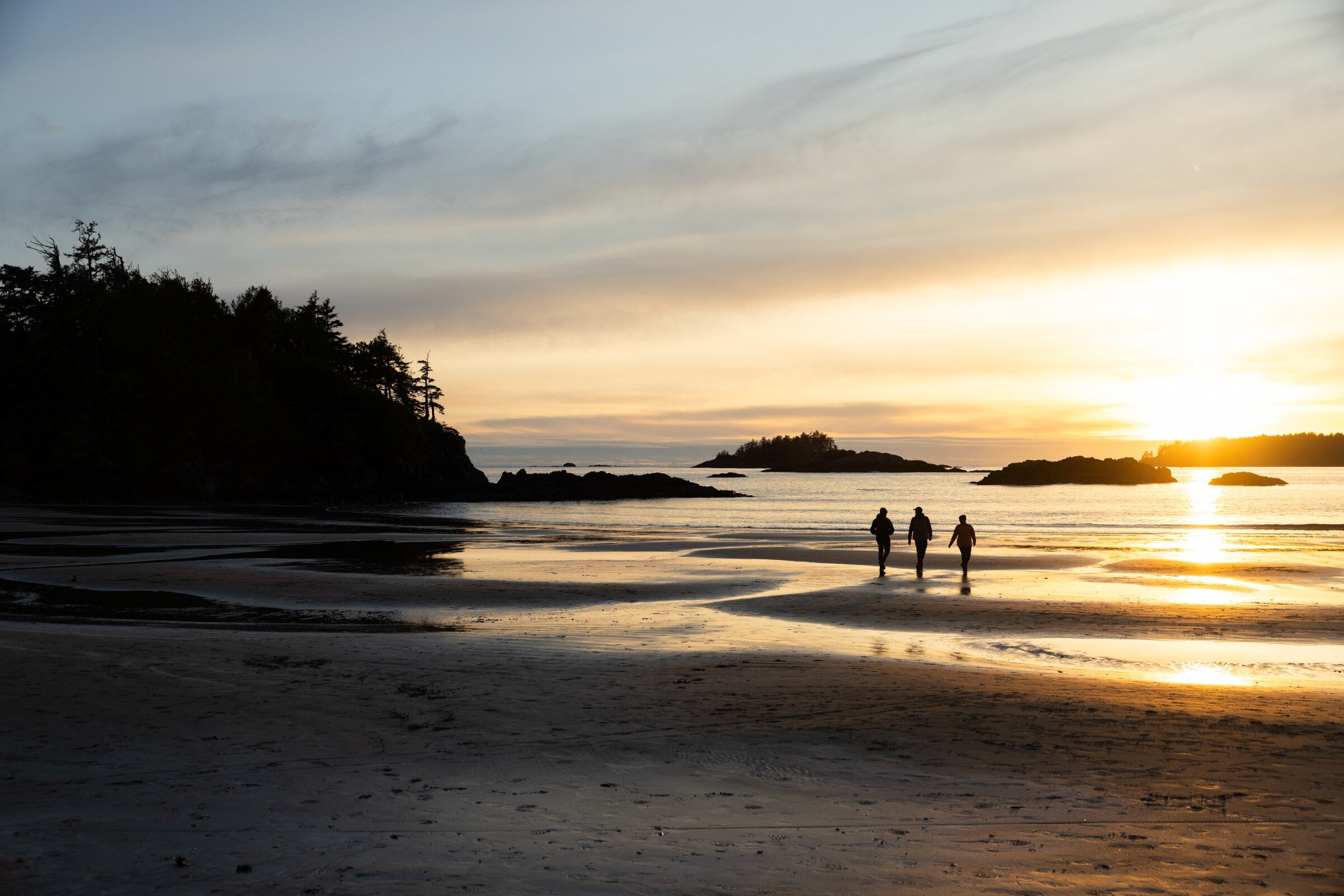 Three people walking along the beach at sunrise